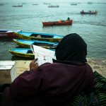 man sitting on lakeshore and reading newspaper
